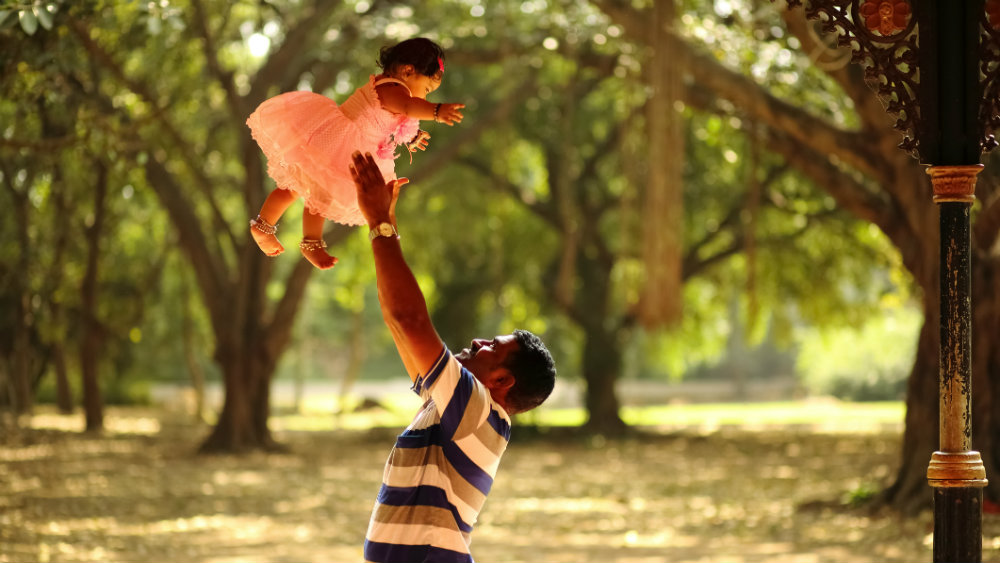 A young man throwing and catching his daughter above his head