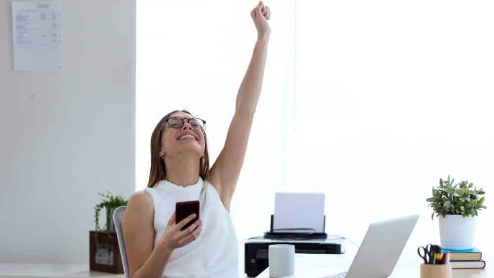 young woman celebrating a victory while working with mobile phone in the office
