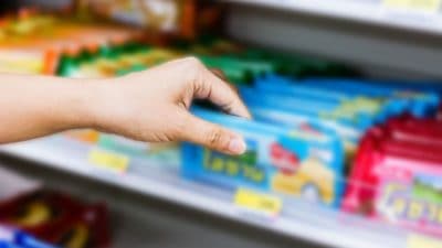 Hand of woman choosing or taking sweet products, snacks on shelves in convenience store