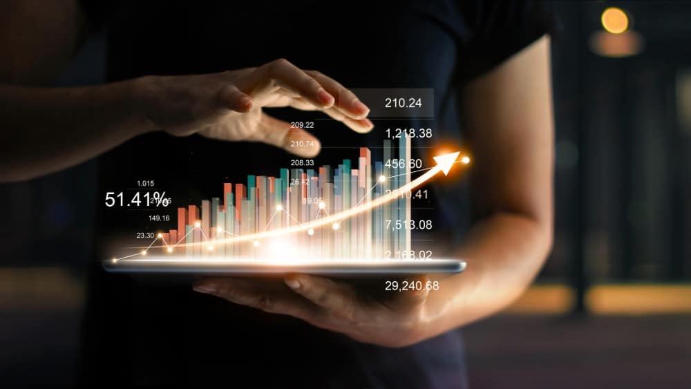 Businessman holding tablet and showing a growing virtual hologram of statistics, graph and chart with arrow up on dark background. Stock market. Business growth, planning and strategy concept