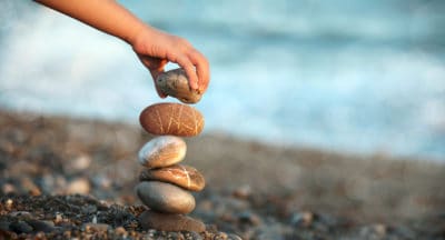 A person builds a rock tower on a beach.