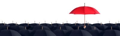 A red umbrella stands higher than a crowd of black umbrellas.