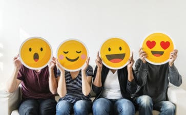 four people hold happy emoji masks