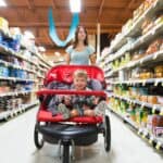 A woman shops in a grocery store while pushing a stroller with a child