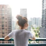 A woman stands on an apartment balcony in a city