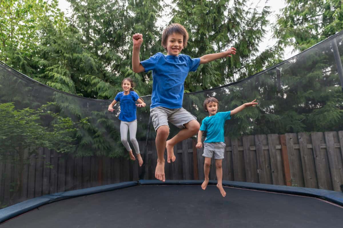 Three children jump on an outdoor trampoline