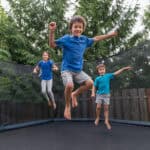 Three children jump on an outdoor trampoline