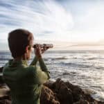 person with spyglass looks at ocean horizon
