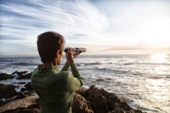person with spyglass looks at ocean horizon