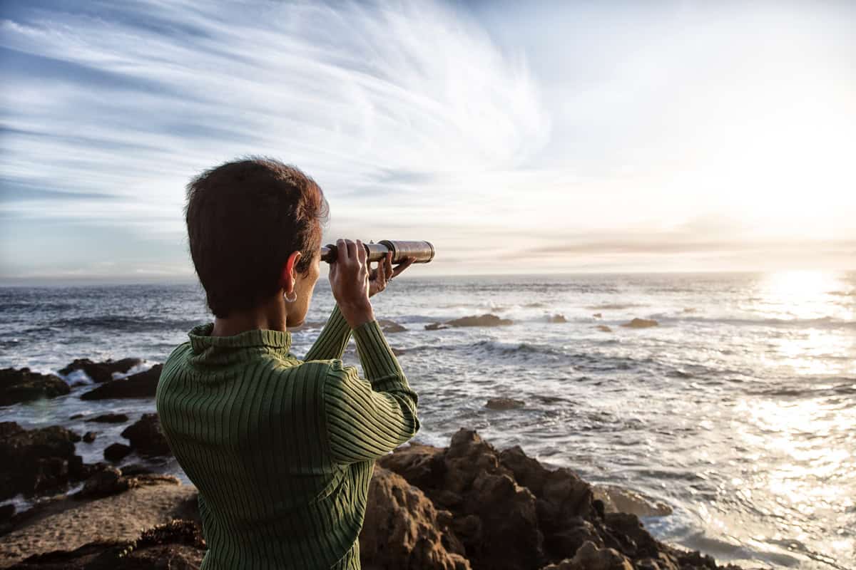 person with spyglass looks at ocean horizon